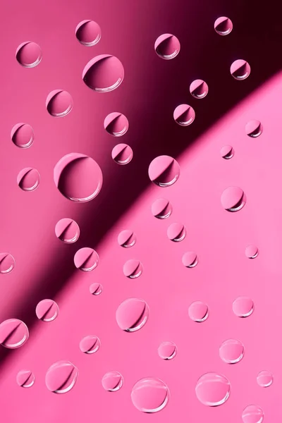 Vue rapprochée de gouttes d'eau calmes transparentes sur fond rose — Photo de stock