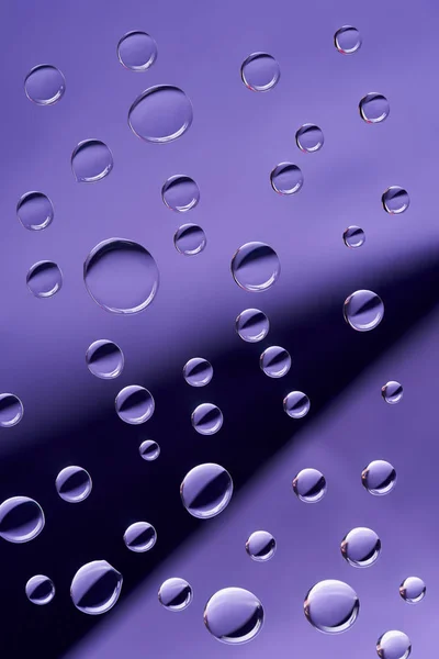 Vista de cerca de gotitas tranquilas transparentes sobre fondo violeta - foto de stock