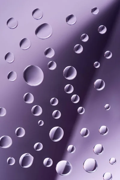 Close-up vista de gotas calmas transparentes no fundo roxo — Fotografia de Stock