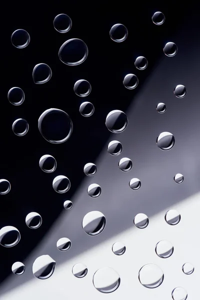 Vista de cerca de gotas de agua transparentes sobre fondo negro, gris y blanco - foto de stock