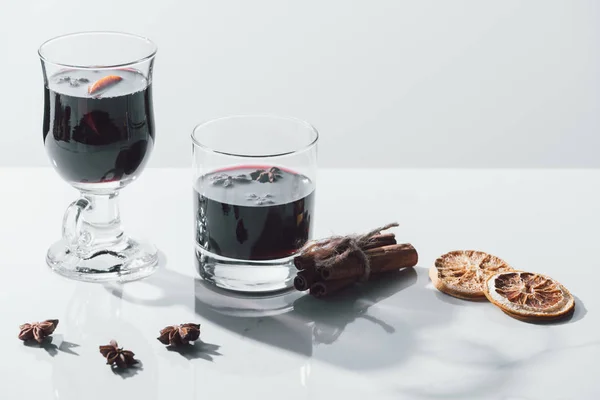 Vin chaud dans des verres et bâtonnets de cannelle sur table blanche — Photo de stock