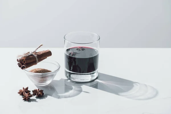 Mulled wine in glass, cinnamon sticks and brown sugar on white tabletop — Stock Photo