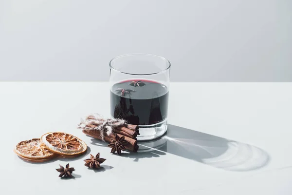 Vin chaud en verre, bâtonnets de cannelle et oranges séchées sur table blanche — Photo de stock