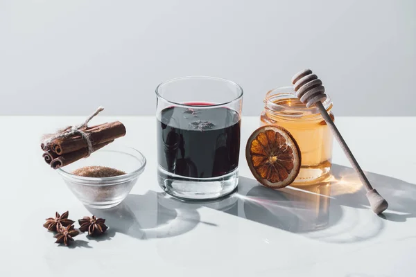 Mulled wine in glass, cinnamon sticks and honey on white tabletop — Stock Photo
