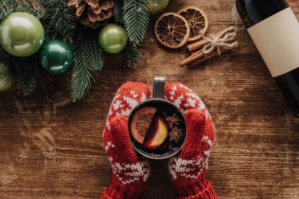 Imagem cortada de mulher segurando xícara de vinho quente à mesa de madeira com galhos de abeto de natal — Fotografia de Stock