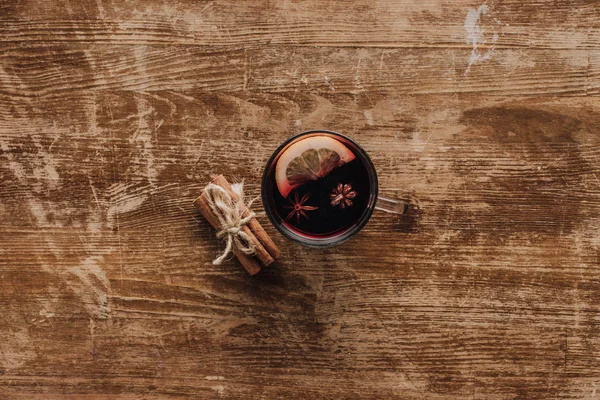 Vista superior da xícara de vinho ruminado e paus de canela na mesa de madeira — Fotografia de Stock