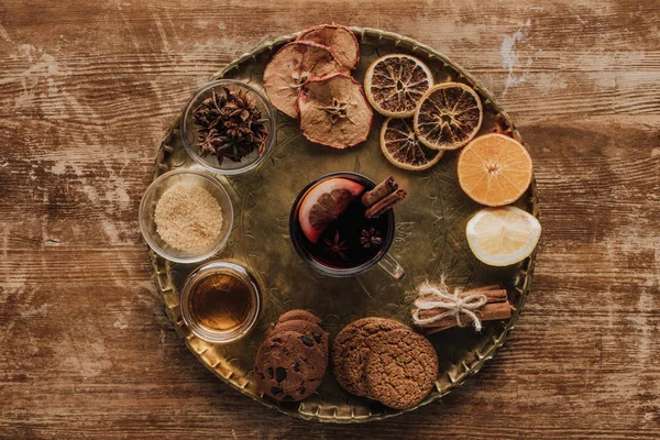 Vista superior del vino caliente en copa y galletas en bandeja redonda sobre mesa de madera - foto de stock