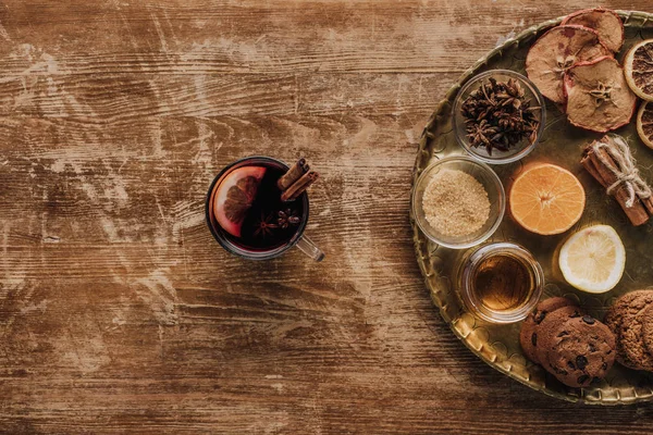 Vista superior de vino caliente en copa y bandeja redonda con dulces en mesa de madera - foto de stock