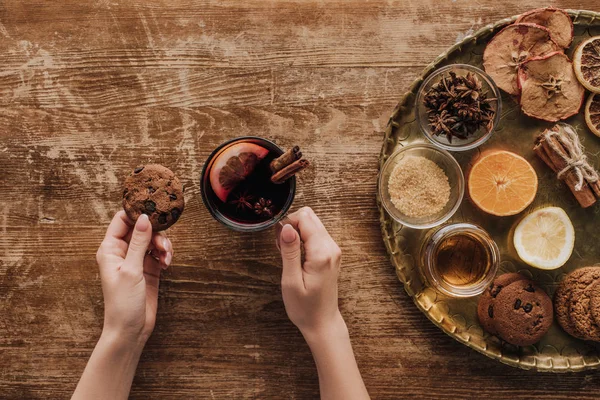 Cropped image of woman holding cup of mulled wine and cookie at wooden table — Stock Photo