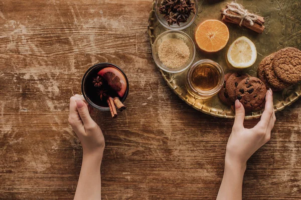Cropped image of woman holding cup of mulled wine and taking cookie from tray — Stock Photo
