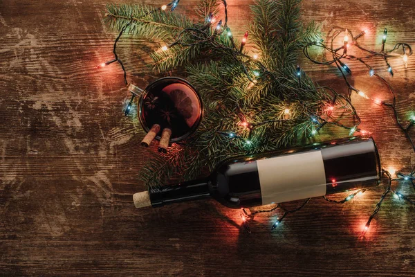 Vista superior de la botella de vino, taza de vino caliente y guirnalda en la mesa de madera, concepto de Navidad - foto de stock