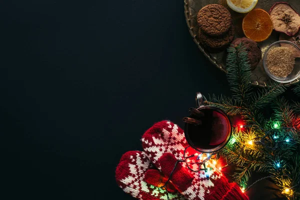 Vista superior de la taza de vino caliente, guirnalda, manoplas y galletas aisladas en negro, concepto de Navidad - foto de stock