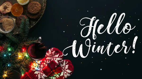 Vista superior de vino caliente en copa, guirnalda y saludo Hola invierno aislado en negro, concepto de Navidad - foto de stock