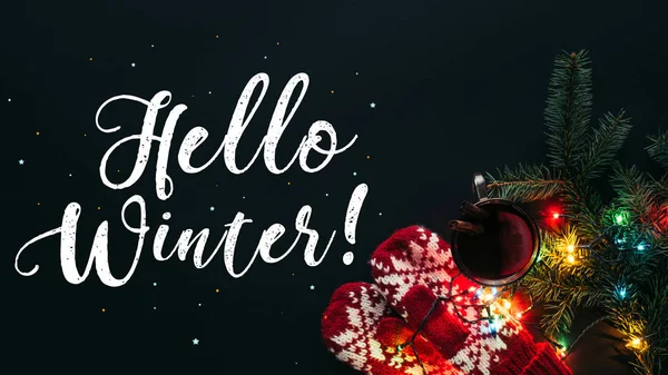 Elevated view of mulled wine in cup, garland and greeting Hello Winter isolated on black, christmas concept — Stock Photo