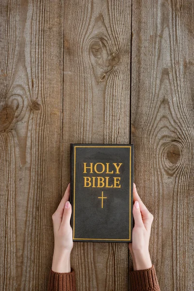 Cropped shot of woman holding holy bible on wooden tabletop — Stock Photo