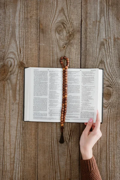 Tiro cortado de mulher com bíblia sagrada e contas em mesa de madeira — Fotografia de Stock