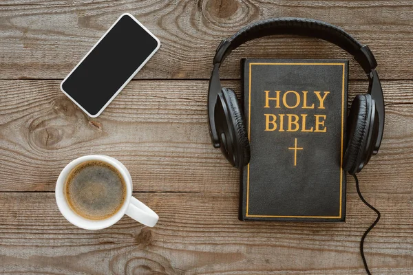 Top view of holy bible with headphones, smartphone and coffee on wooden tabletop — Stock Photo