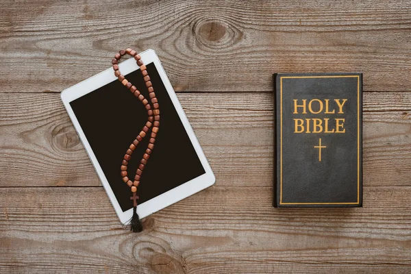 Vista superior de la tableta con cuentas y la Biblia santa acostado en la mesa de madera - foto de stock