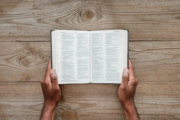 Cropped shot of man holding holy bible over wooden table — Stock Photo