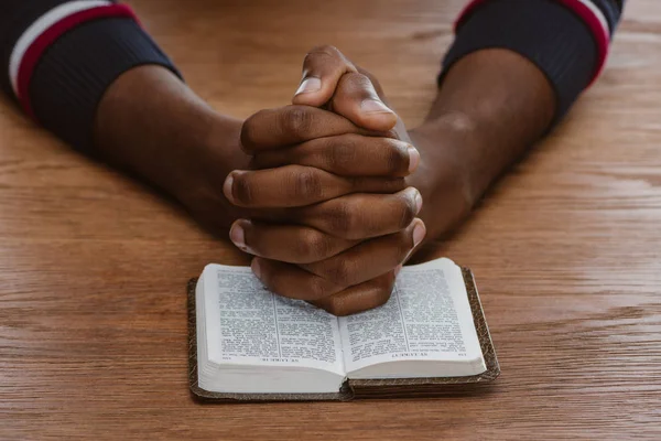 Recortado disparo de hombre afroamericano rezando con la sagrada Biblia - foto de stock