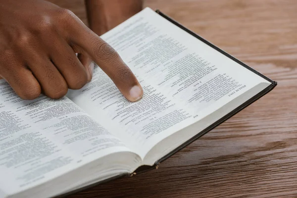 Tiro recortado de homem afro-americano lendo bíblia sagrada e apontando para salmo — Fotografia de Stock