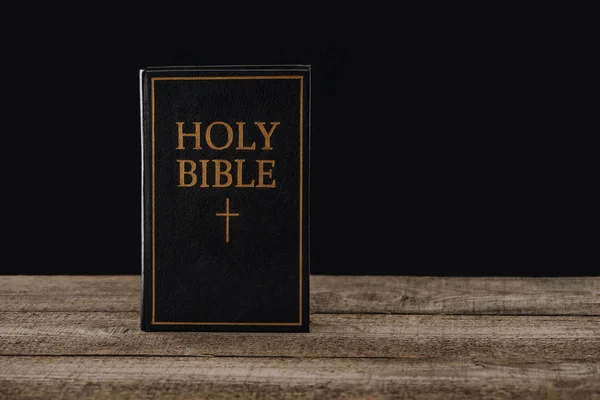 Close-up shot of holy bible standing on wooden table isolated on black — Stock Photo