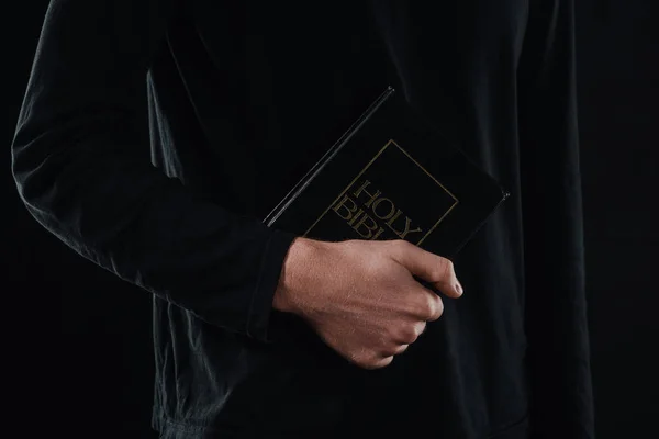 Cropped shot of priest holding holy bible isolated on black — Stock Photo