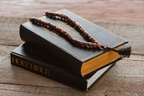Close-up shot of stacked bible books with beads on wooden surface — Stock Photo