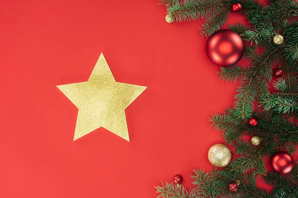 Flat lay with pine tree branches with red and golden christmas balls and golden star isolated on red — Stock Photo