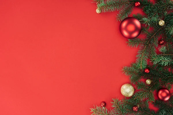 Tendido plano con ramas de pino con bolas de Navidad rojas y doradas aisladas en rojo - foto de stock