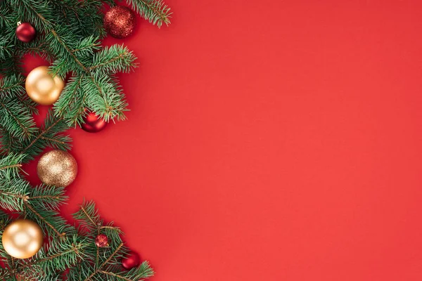Tendido plano con ramas de pino con bolas de Navidad rojas y doradas aisladas en rojo - foto de stock