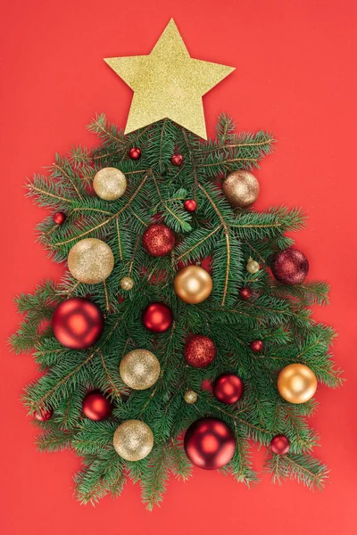 Vista superior de ramas de pino, estrella dorada y bolas de navidad dispuestas en árbol de navidad aislado en rojo - foto de stock