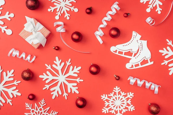 Posa piatta con fiocchi di neve decorativi bianchi, nastri, giocattoli di Natale rossi e regalo avvolto isolato su rosso — Foto stock