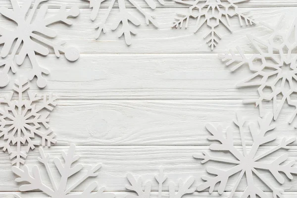 Tendido plano con copos de nieve decorativos sobre mesa de madera blanca con espacio en blanco en el centro - foto de stock
