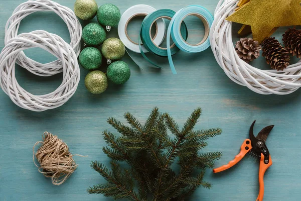 Vista superior de las ramas de pino y decoraciones para la corona de Navidad hecha a mano en la mesa de madera azul - foto de stock