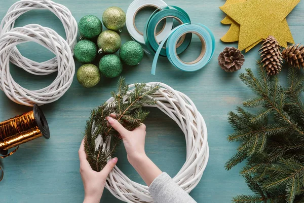 Teilansicht einer Frau, die handgefertigten Weihnachtskranz auf blauer Holztischplatte macht — Stockfoto