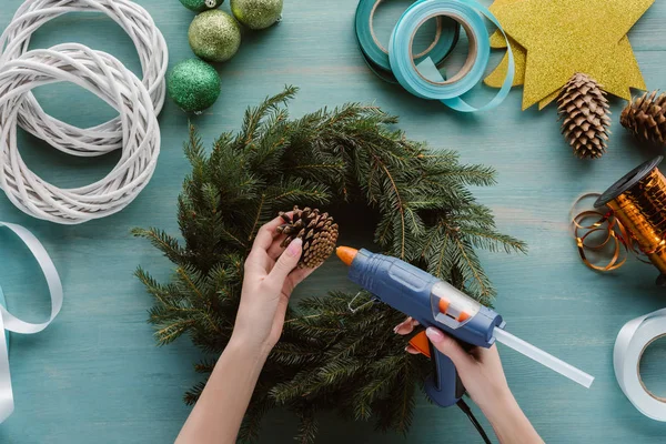 Plan recadré de femme décorant couronne de Noël à la main avec cône de pin sur la surface en bois bleu — Photo de stock