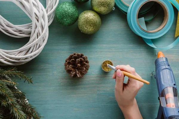 Teilansicht der Frau, die Tannenzapfen mit goldener Farbe auf blauer Holzoberfläche färbt — Stock Photo