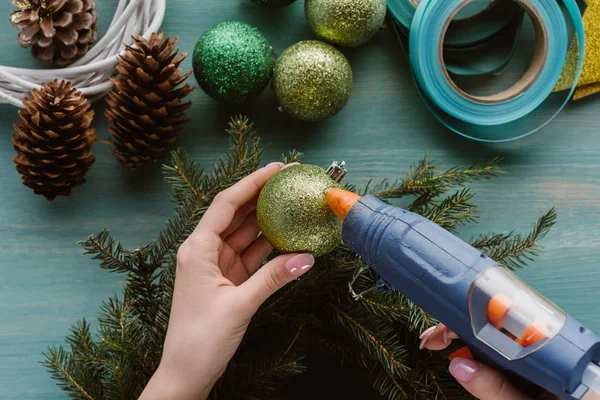 Visão parcial da mulher que decora a grinalda de pinho artesanal com brinquedos de Natal na superfície de madeira azul — Fotografia de Stock