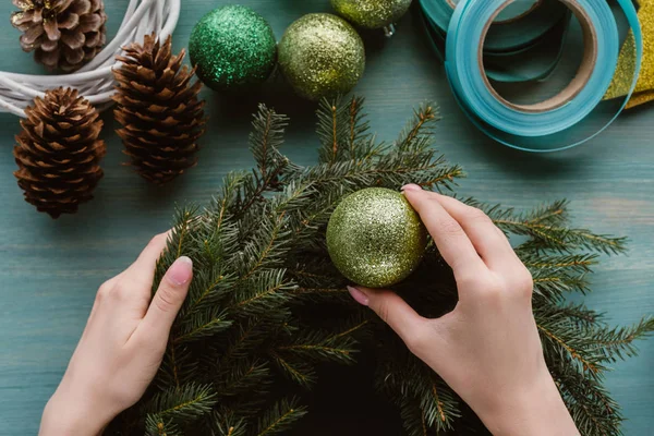 Vista parziale della donna decorazione a mano ghirlanda di pino con giocattoli di Natale sulla superficie di legno blu — Foto stock