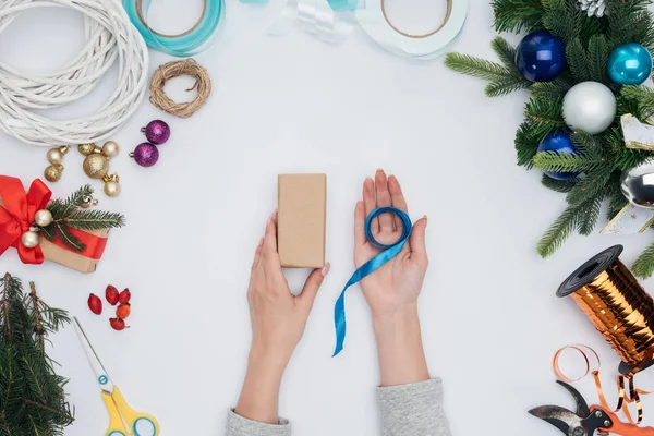 Teilansicht der Frau mit blauem Band und eingewickeltem Weihnachtsgeschenk in den Händen isoliert auf weiß — Stockfoto