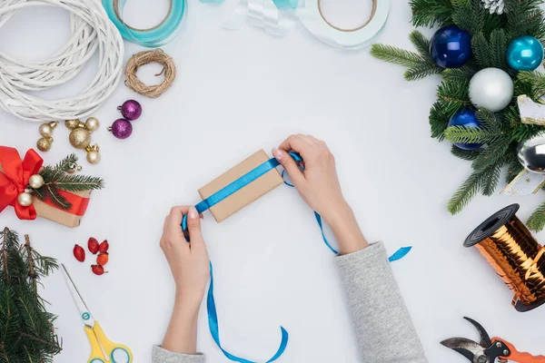 Cropped shot of woman wrapping christmas gift with blue ribbon isolated on white — Stock Photo