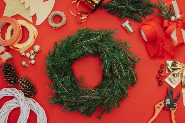 Flat lay with pine tree branches arranged in circle and decorations for christmas wreath isolated on red — Stock Photo