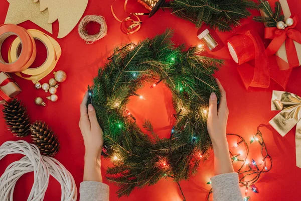 Partial view of woman holding handmade christmas wreath with lights on red background — Stock Photo