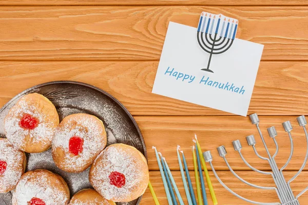 Cama plana con donuts, velas, menorah y feliz tarjeta hannukah en la superficie de madera, concepto hannukah - foto de stock