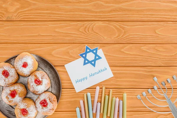 Flat lay with doughnuts, candles, menorah and happy hannukah card on wooden surface, hannukah concept — Stock Photo