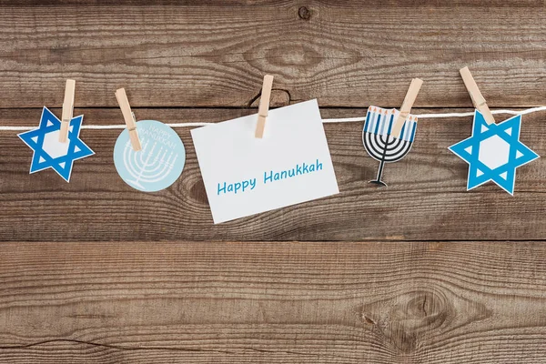 Top view of happy hannukah card and holiday paper signs pegged on rope on wooden tabletop, hannukah concept — Stock Photo