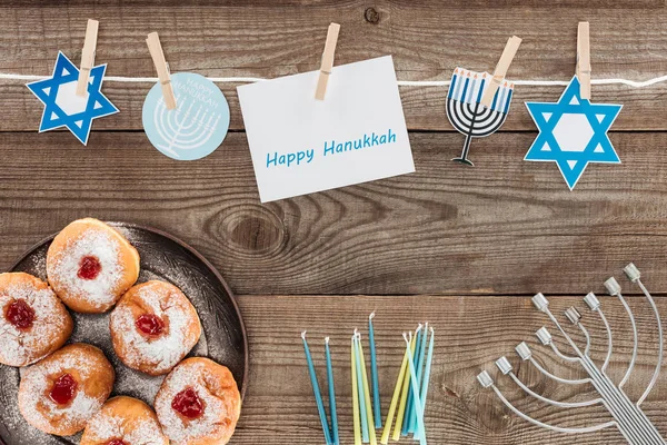 Plat étendu avec des beignets, des bougies, menorah et carte heureuse hannukah sur la surface en bois, concept hannukah — Photo de stock
