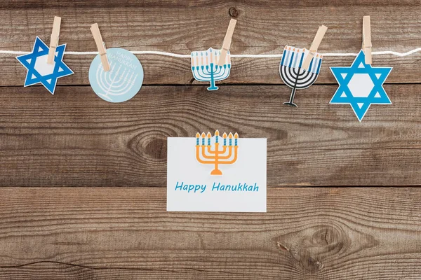 Cama plana con tarjeta feliz hannukah y carteles de papel de vacaciones pegados a la cuerda en la mesa de madera, concepto hannukah - foto de stock