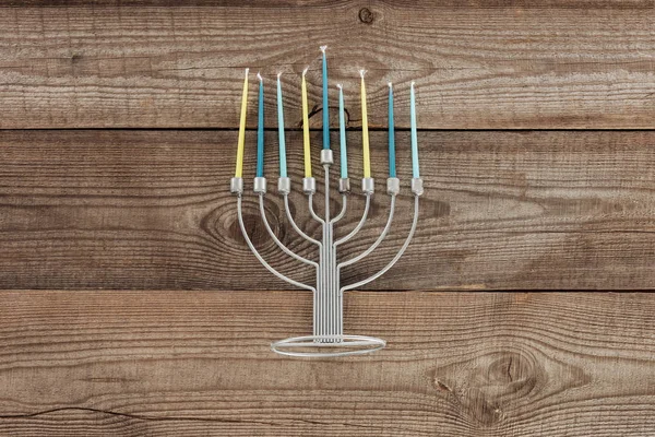 Top view of traditional jewish menorah with blue and yellow candles on wooden tabletop, hannukah holiday concept — Stock Photo